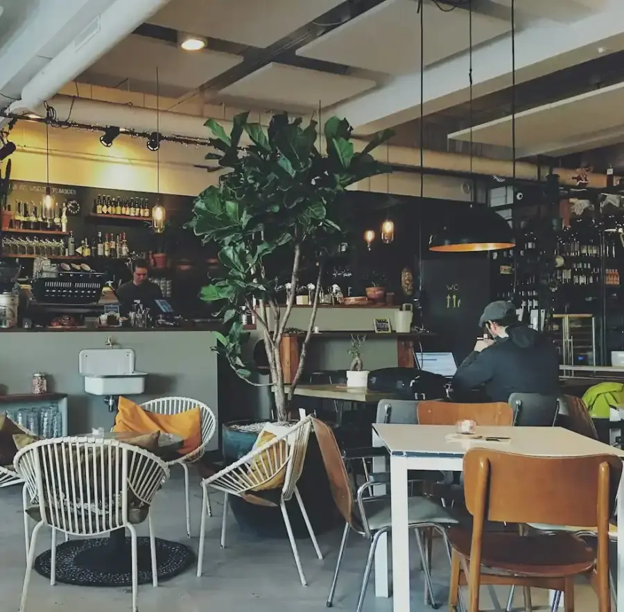 Independent café interior with tables, plants and a service counter.
